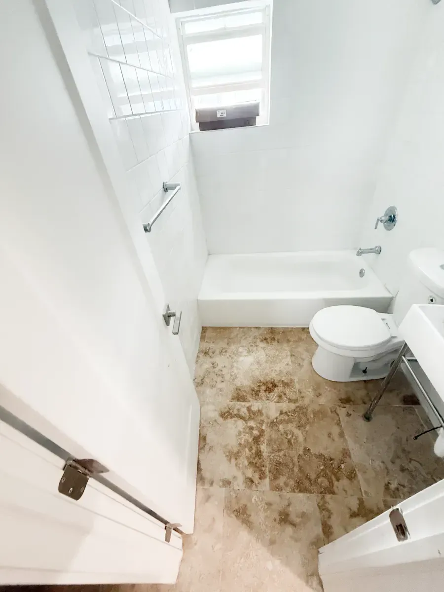 A small bathroom featuring a white bathtub, toilet, sink, and mottled brown tile flooring.