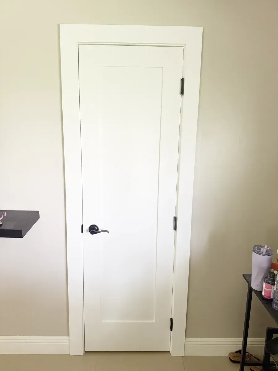 A white, single-panel interior door with matte black hardware, set in a light beige room with white trim.