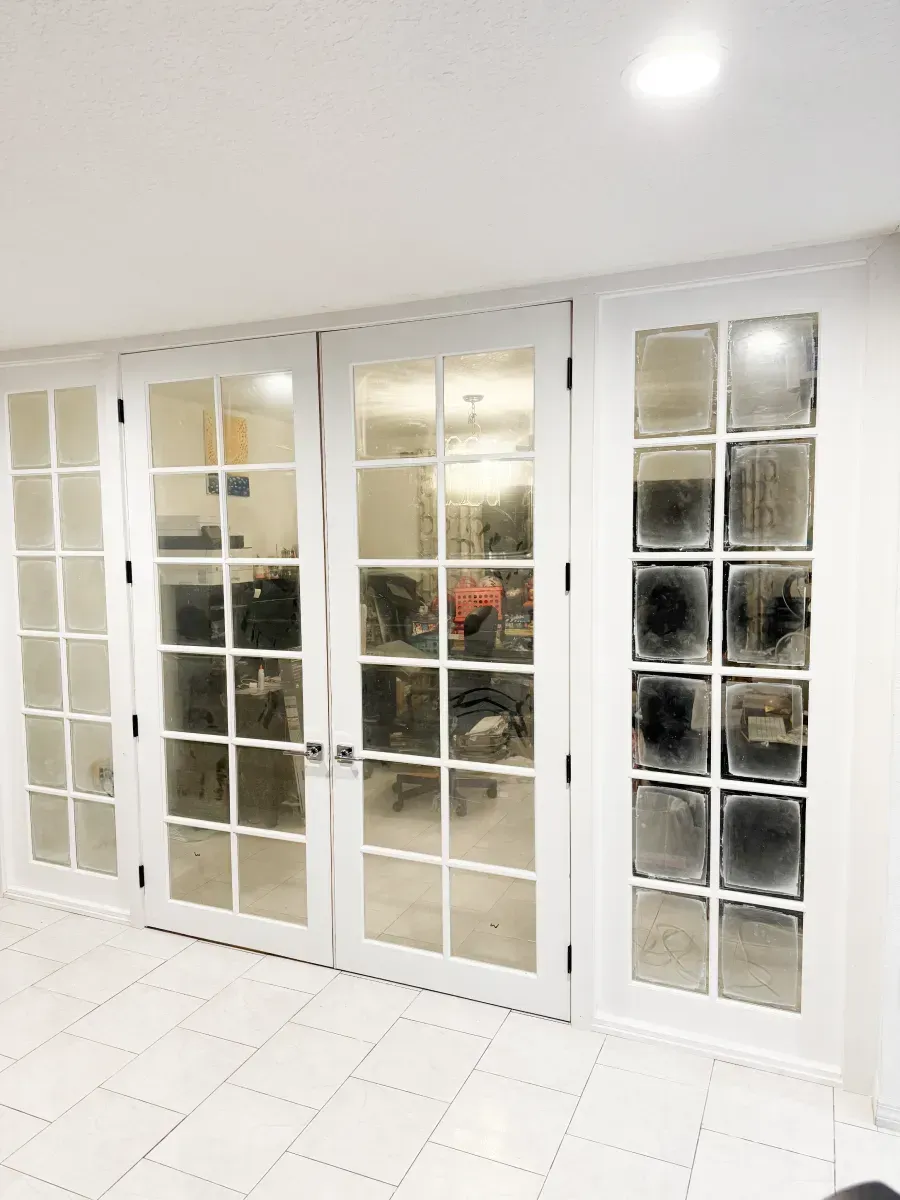 A set of four white-framed glass paneled doors installed in a row against a white wall with a tiled floor.