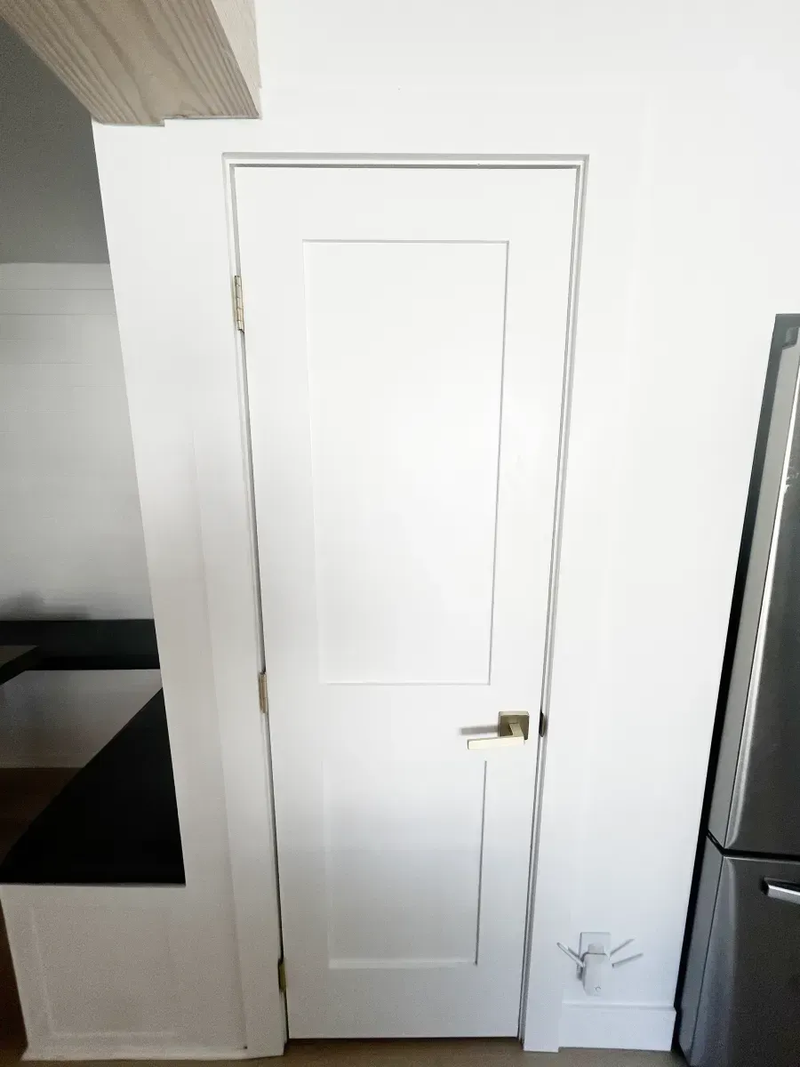 A white interior door with two rectangular panels and a brass handle set in a white wall next to a seating area.