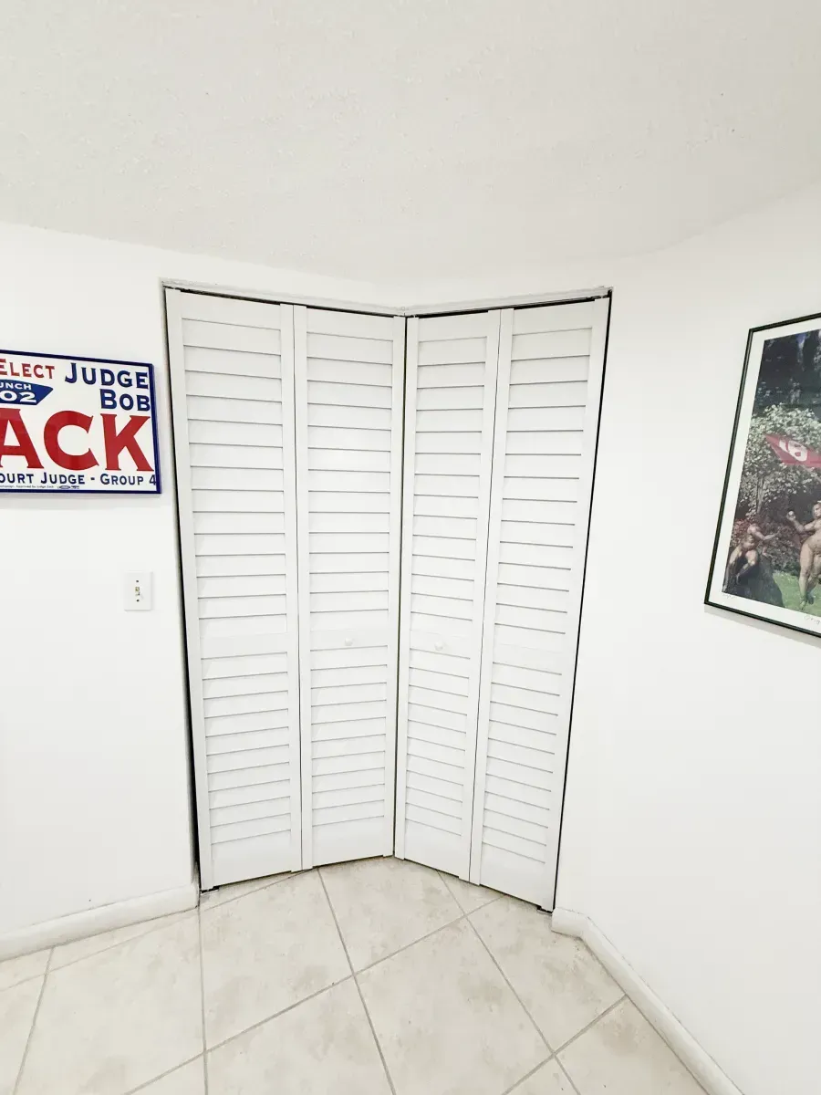 White bi-fold louvered doors installed in a corner, flanked by wall art on a white tiled floor.