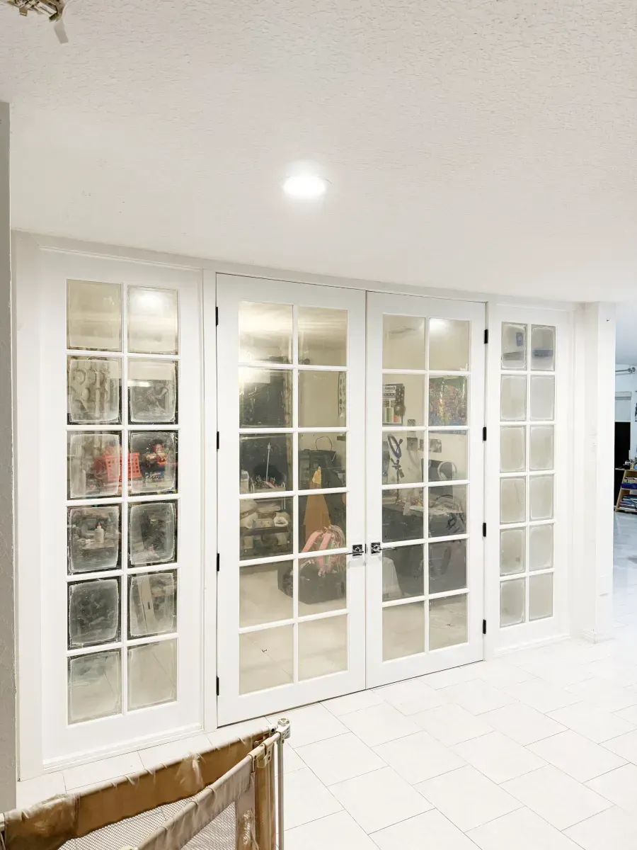 A set of white-framed glass French doors installed in a bright room with white tile flooring.