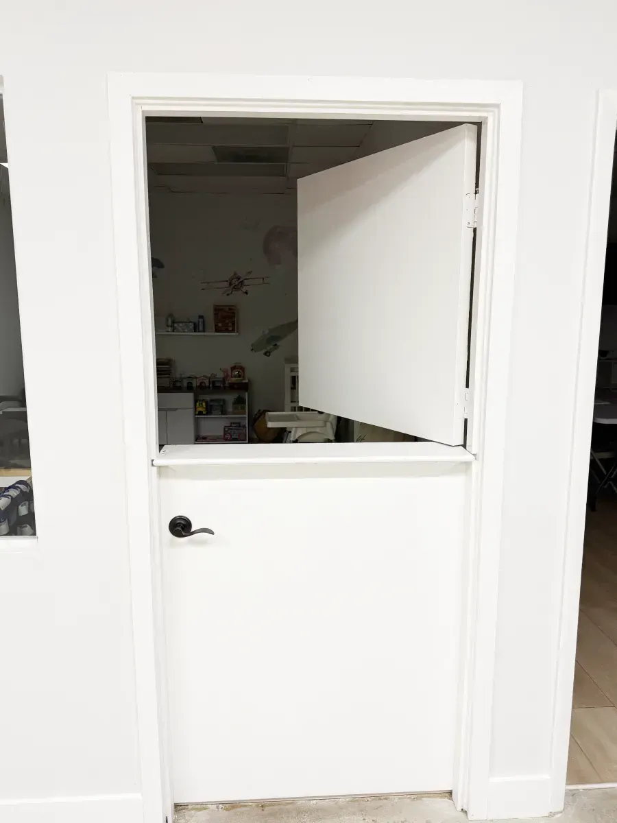 A white Dutch door installed in a doorway, with the top half open and the bottom half closed.