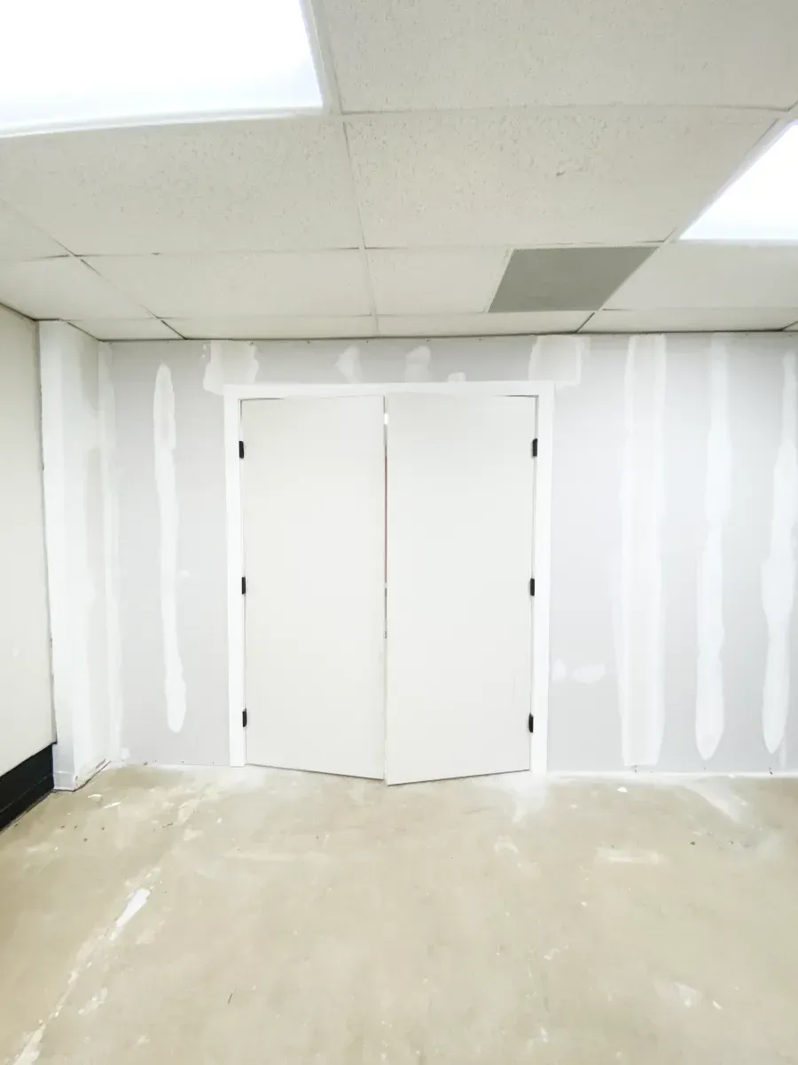 A room with unfinished drywall walls featuring vertical taped seams and a central set of closed white double doors.