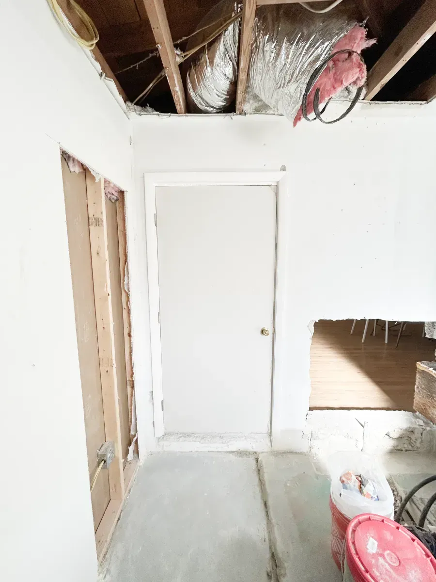 A partially renovated interior space showing exposed ceiling joists, a doorway, an open wall stud, and construction debris.