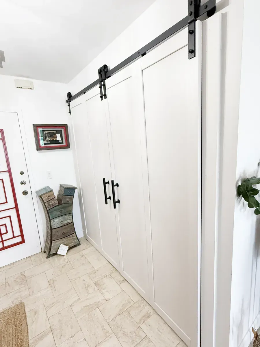 White sliding barn doors with black hardware and handles installed along a light-colored wall in a bright indoor space.