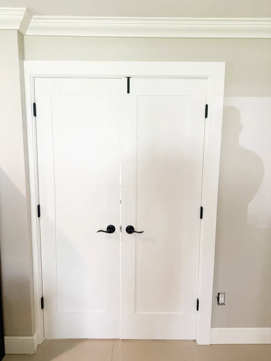 White double doors with black hardware, centered in a room with light-colored walls and crown molding.