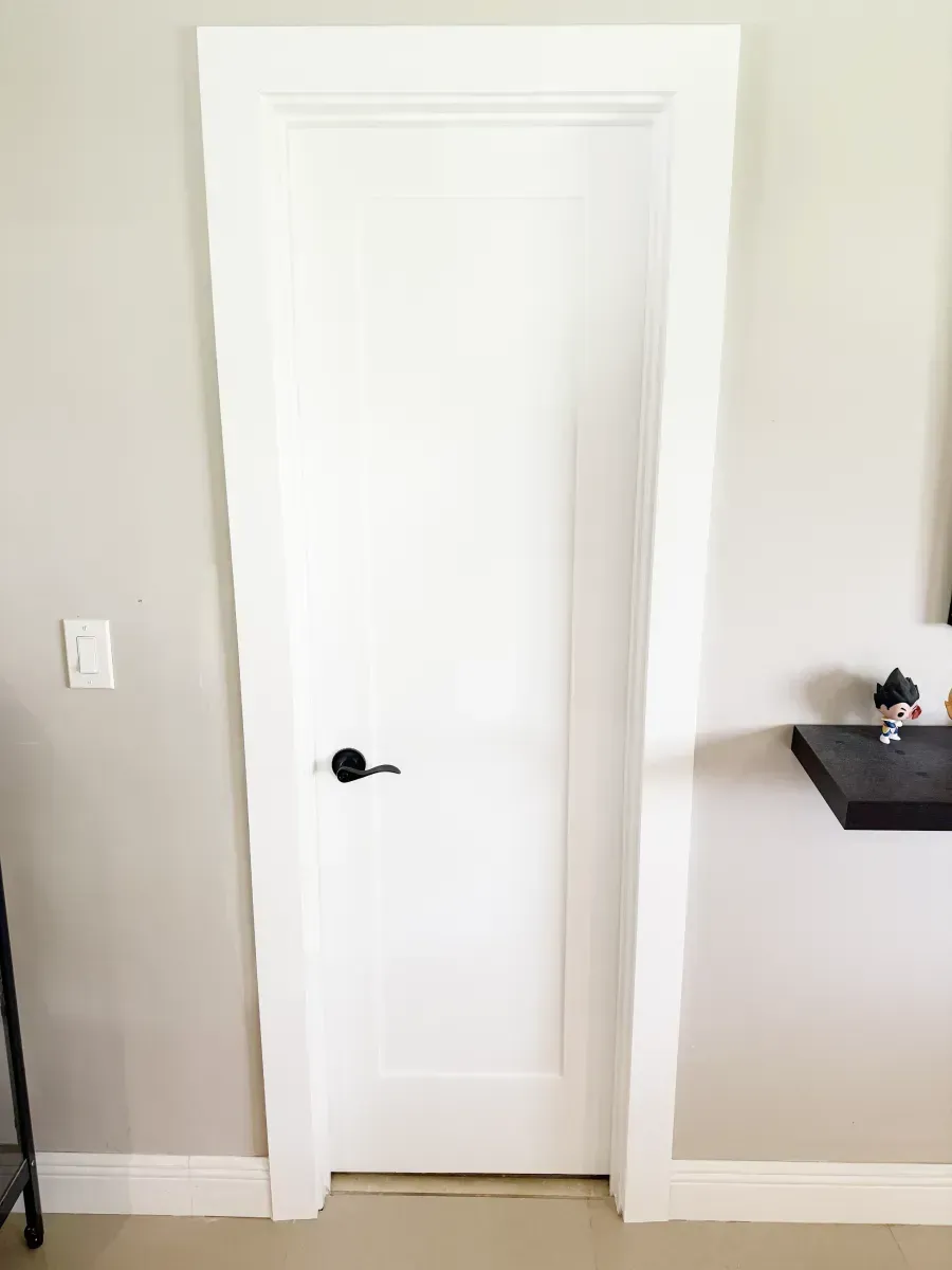 A white, single-panel interior door with black hardware, set within white trim against a light gray wall.