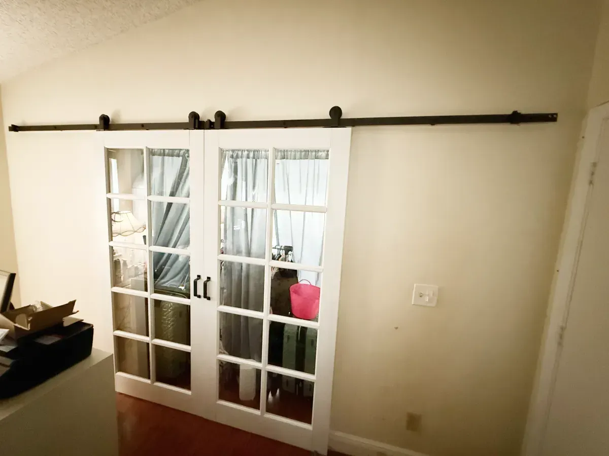 A white, glass-paned sliding barn door mounted on a black metal track against a beige wall.