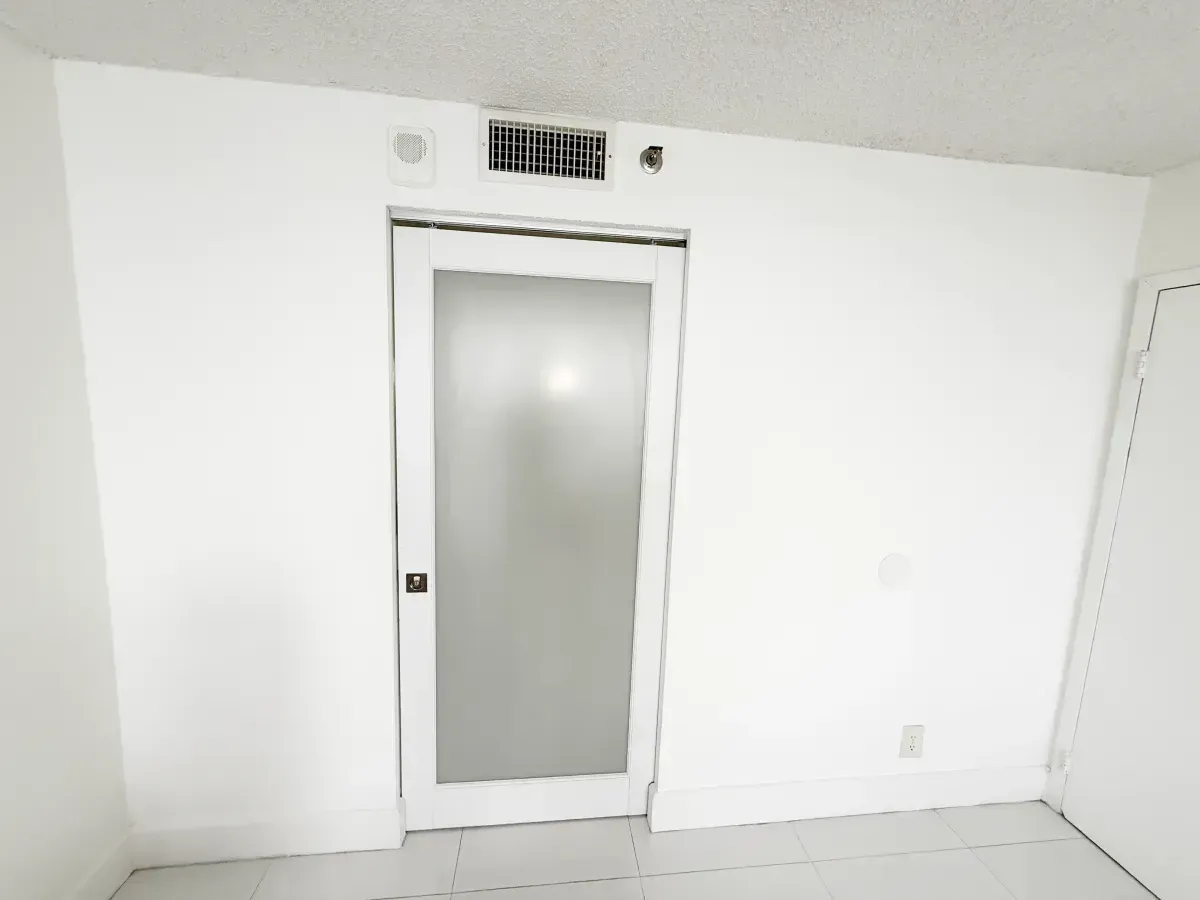 A white, frosted-glass interior door centered in a white wall with an air vent above and a floor-level electrical outlet.