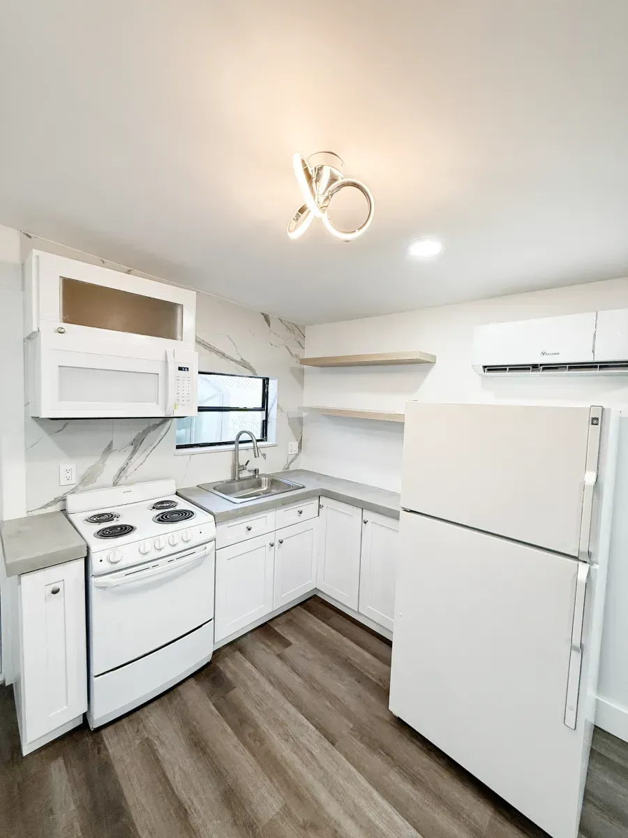 A compact, modern kitchen featuring white cabinets, a white stove, a white refrigerator, and light wood plank flooring.