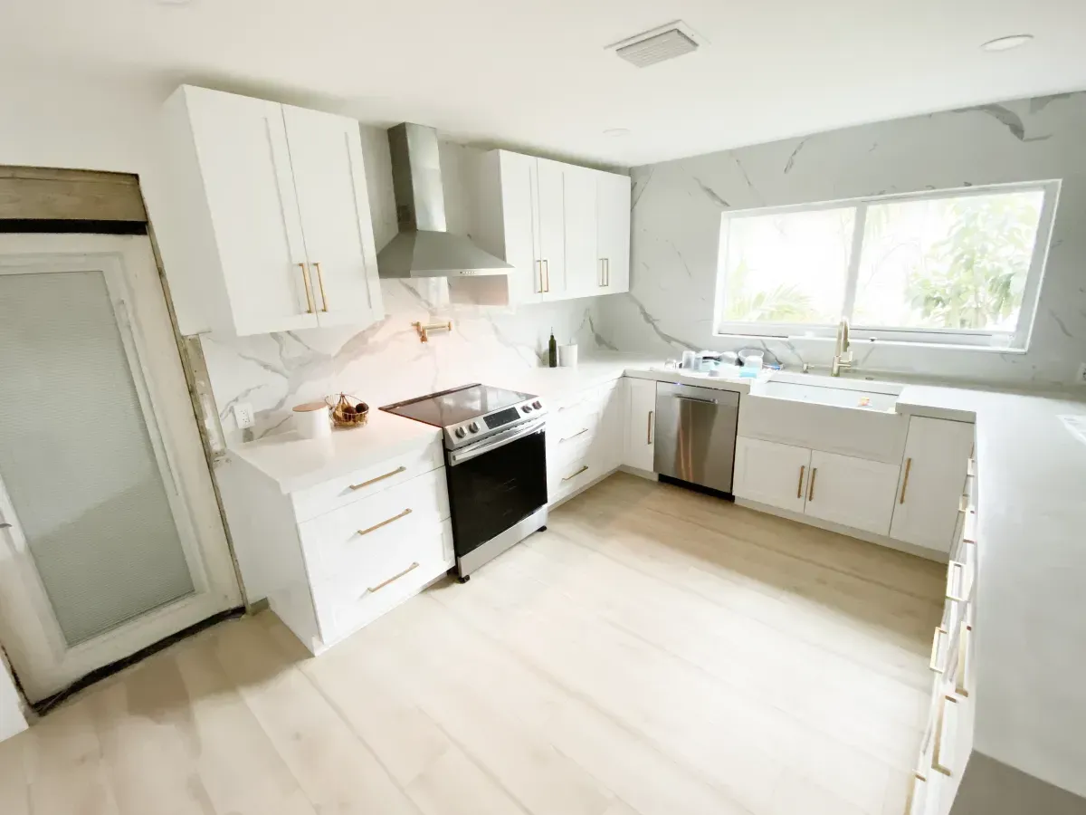 A bright, modern kitchen featuring white cabinets, stainless steel appliances, marble-patterned backsplash, and light wood.