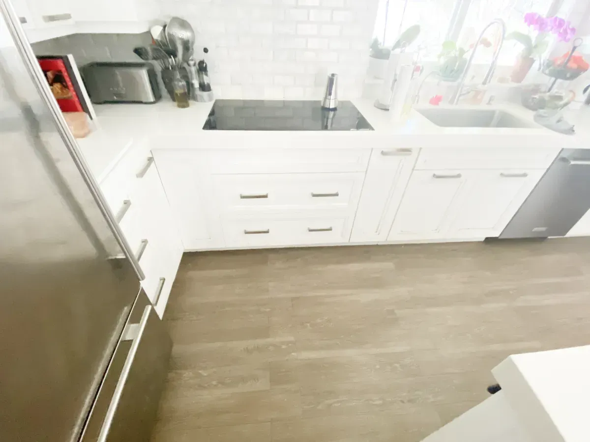 A modern kitchen featuring white cabinets, a black stovetop, a white tiled backsplash, and light wood-tone flooring.