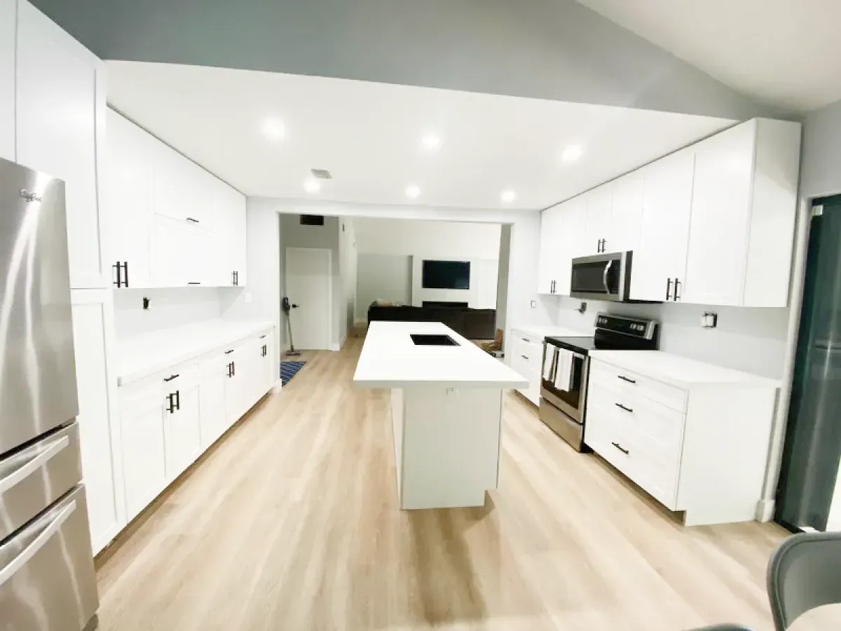 Modern white kitchen with a center island, stainless steel appliances, and light wood flooring.