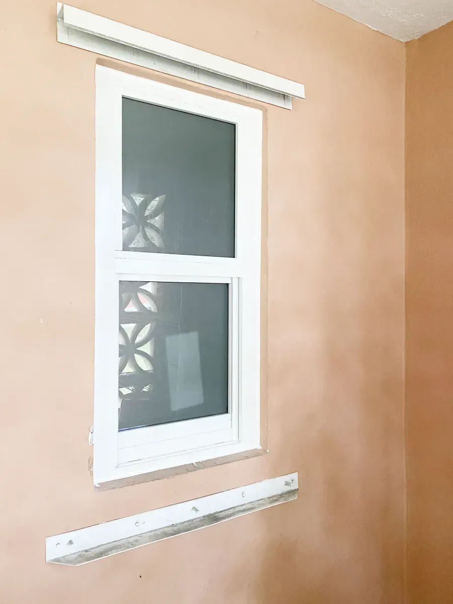 A window centered on a light peach-colored wall with white curtain rod brackets mounted above and below the window frame.