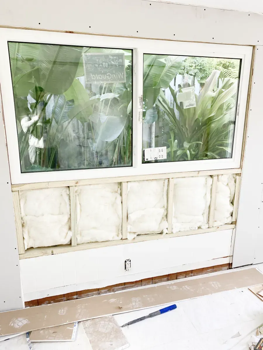 A white-framed window installed above an unfinished wall section with exposed wood studs, insulation, and drywall edges.