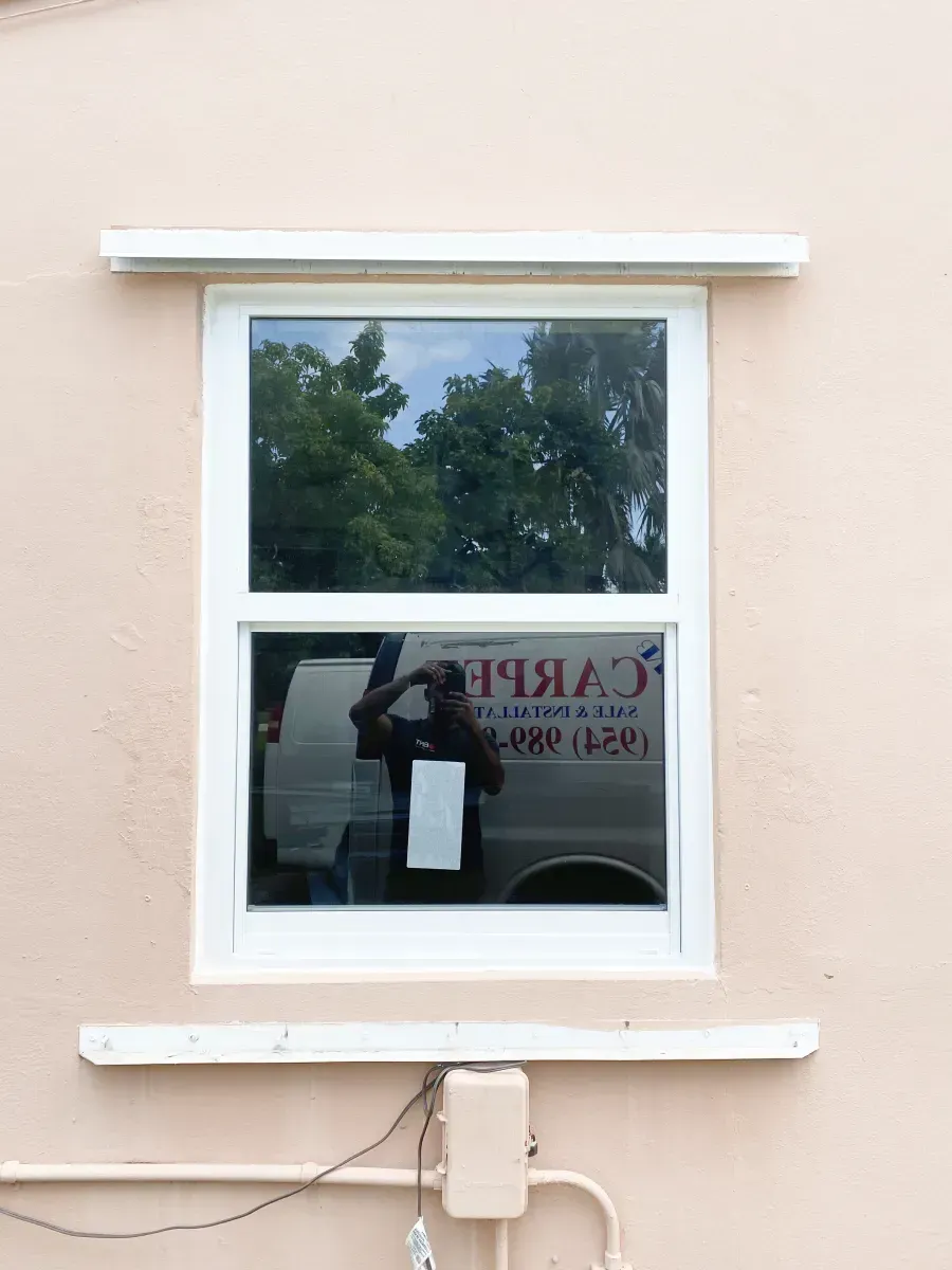 A white window frame set in a peach-colored wall, with a reflection of a service vehicle and a person in the glass.