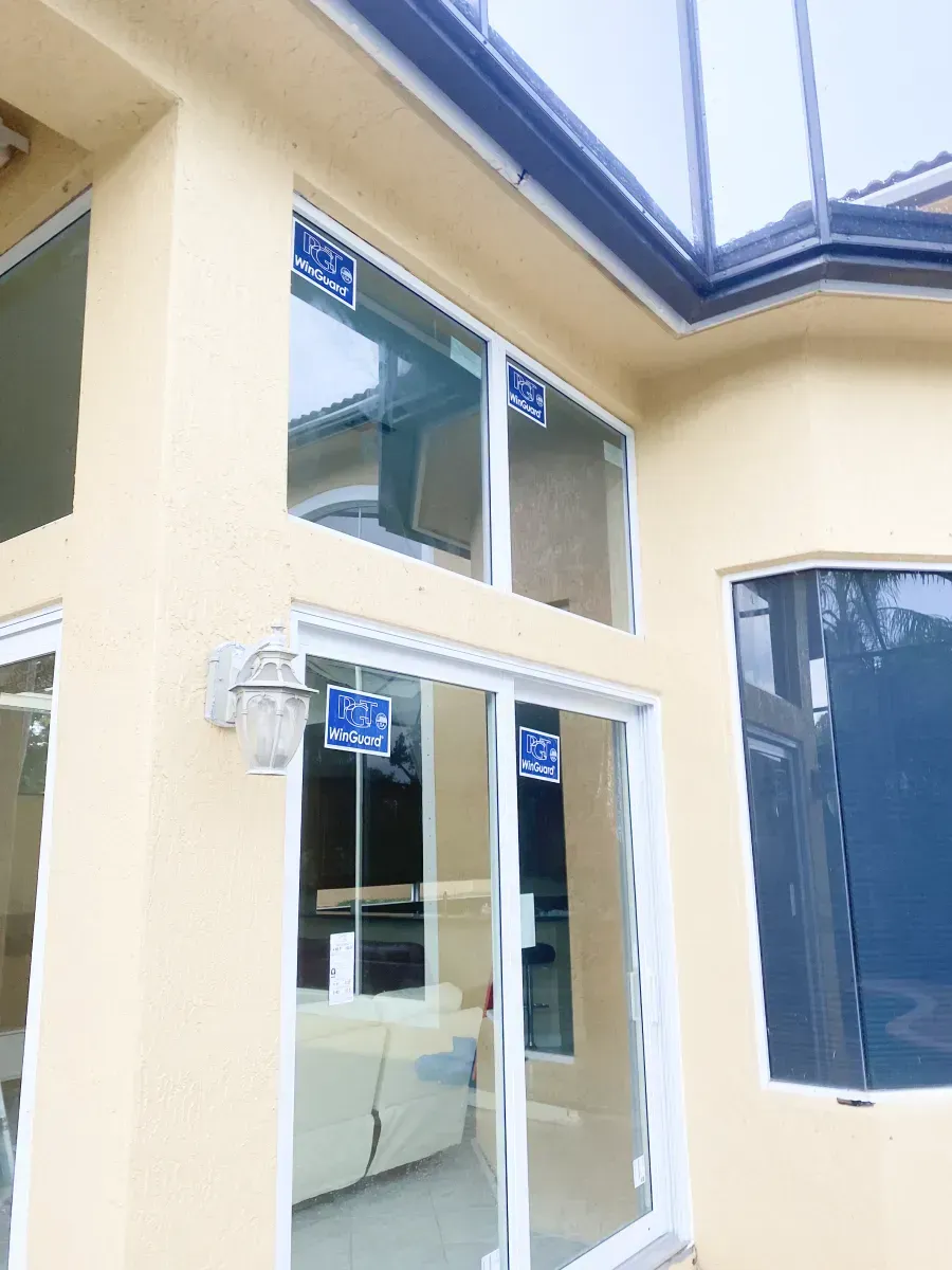 Exterior view of a cream-colored home with a large sliding glass door and windows, showing blue labels on the glass.