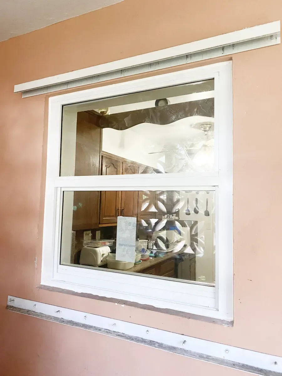 A white window installed on a peach-colored wall with metal tracks mounted above and below the frame.