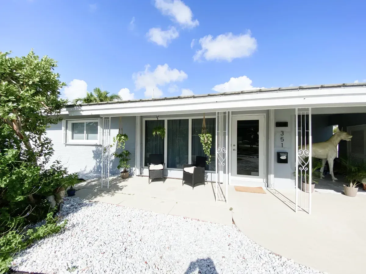 A light-gray single-story house with a covered front porch, white rock landscaping, and a large dog statue on the right.
