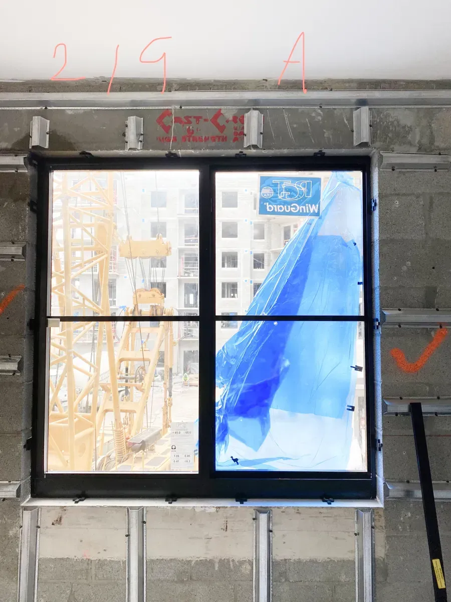 A newly installed black-framed window in a partially finished wall with construction marks and tape in a room.