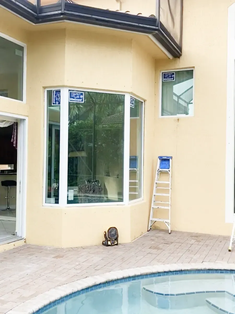 A tan exterior wall with new windows, a stepladder, and part of a swimming pool in the foreground.