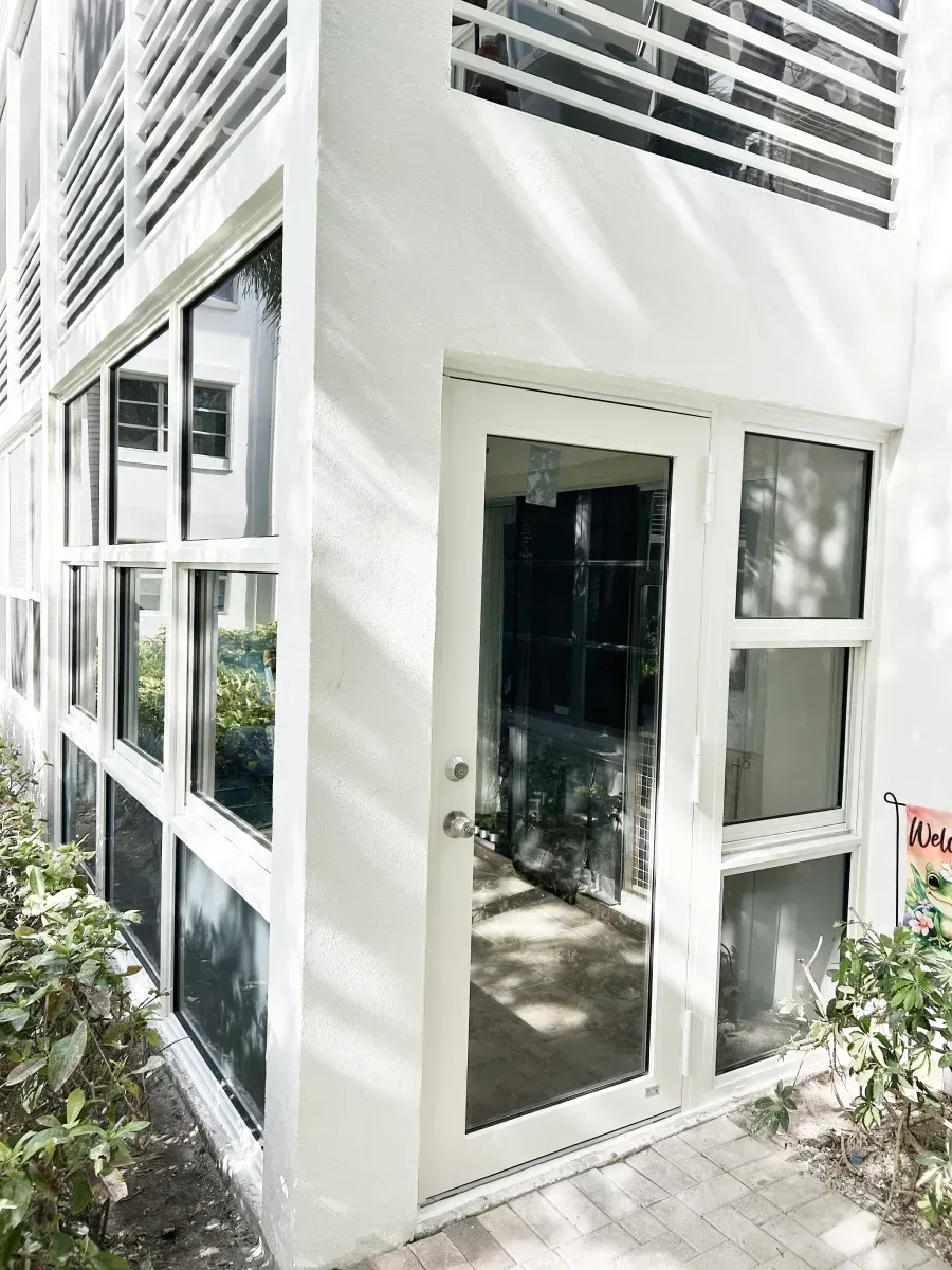 A bright white building exterior featuring a glass-paned door, adjacent windows, and tiered horizontal architectural beams.