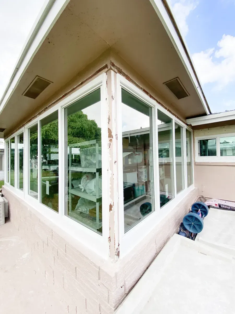 A corner view of a building exterior featuring large glass windows with frames showing signs of paint wear.