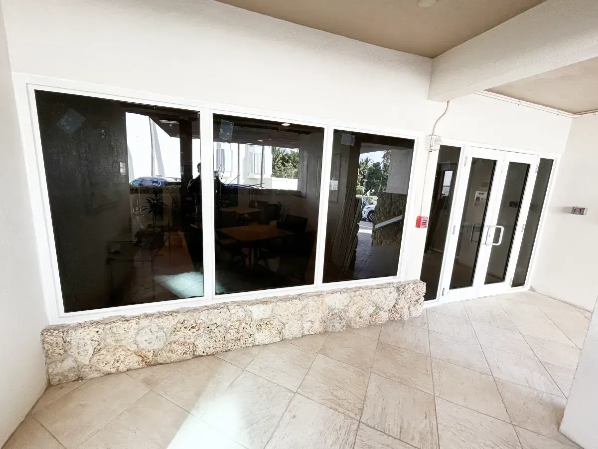 A patio with beige tiled flooring, a stone-accented base, and large glass windows and doors reflecting the surroundings.