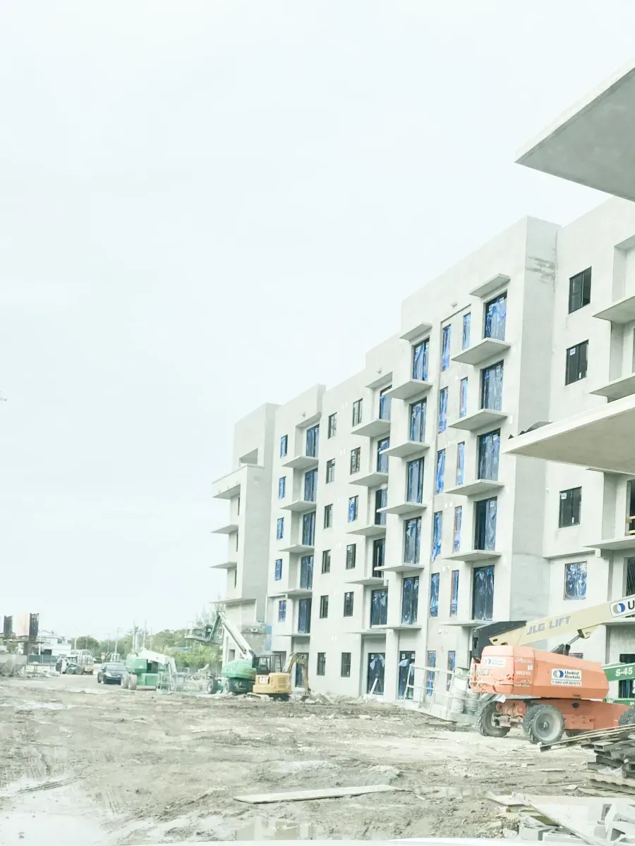A multi-story apartment building under construction with exposed concrete, balconies, and machinery on a dirt lot.