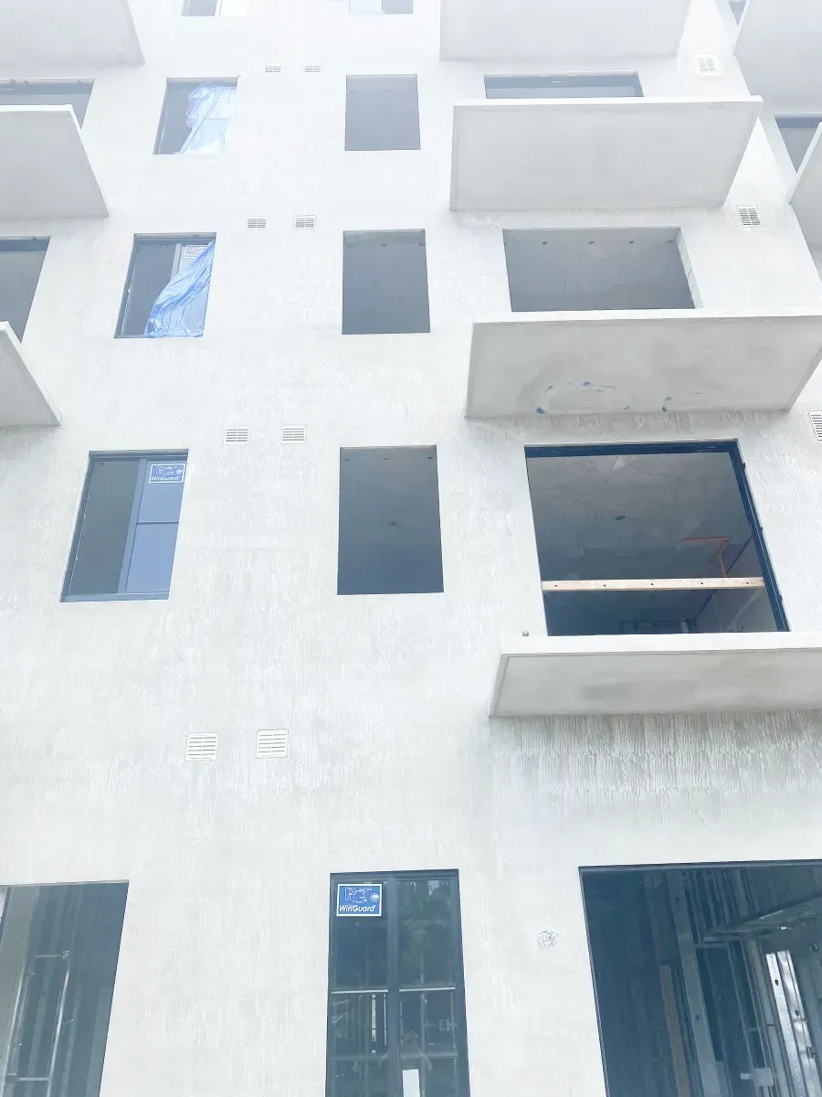 A low-angle view of a grey concrete building under construction with multiple balconies and open window frames.