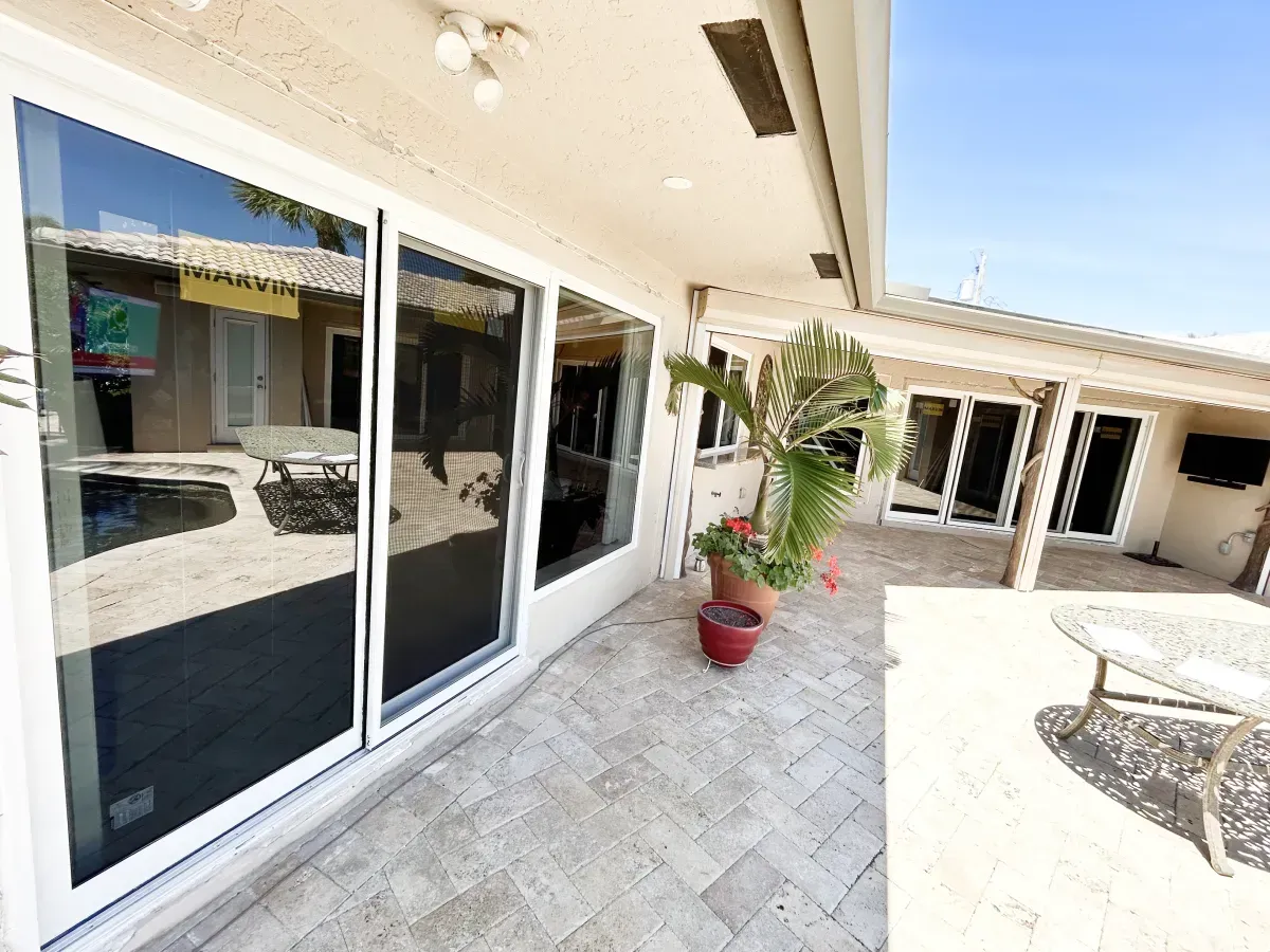 A bright patio area with travertine pavers, large glass sliding doors, a potted plant, and outdoor furniture.