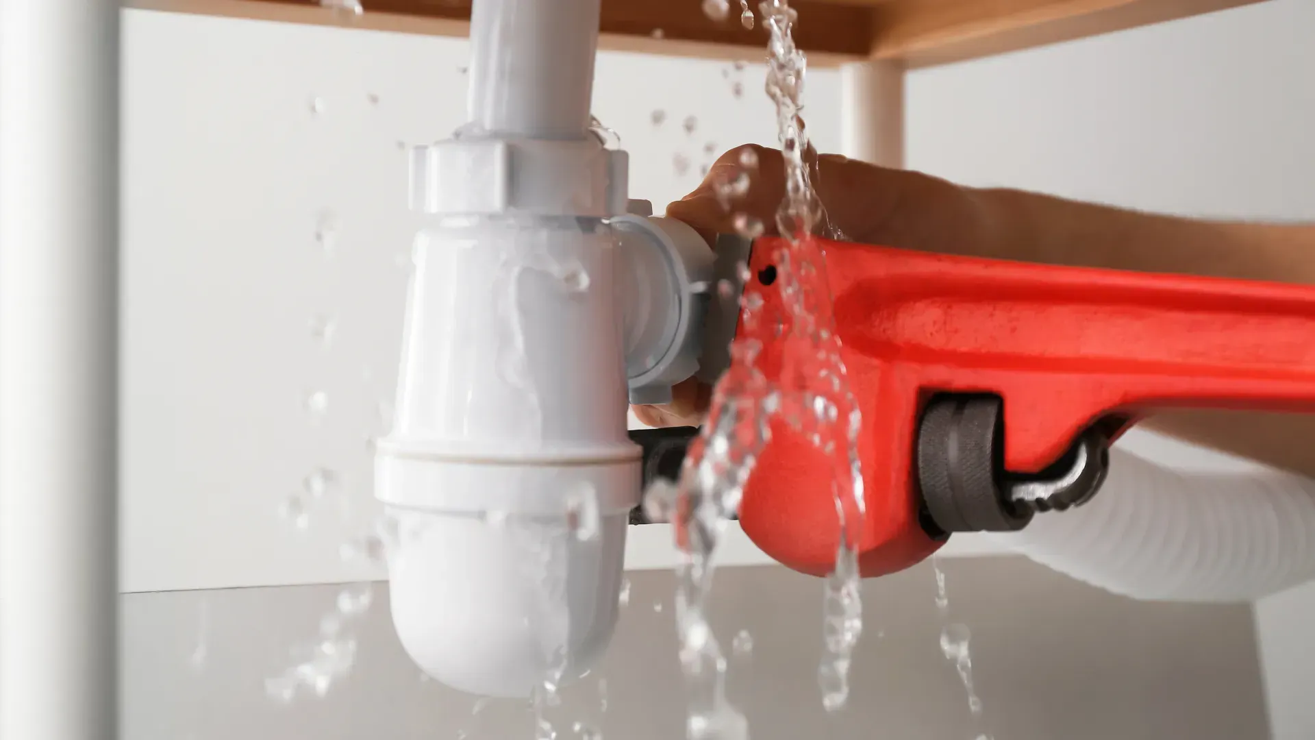 A person is fixing a leaking sink pipe with a wrench.