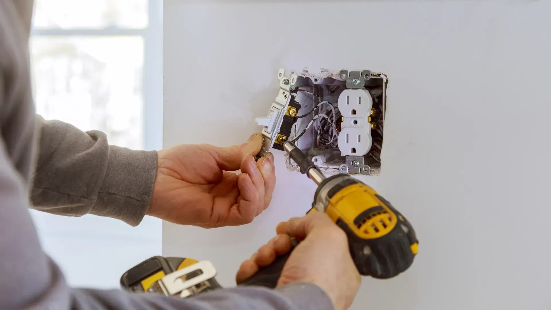 A man is installing a light switch on a wall with a drill.
