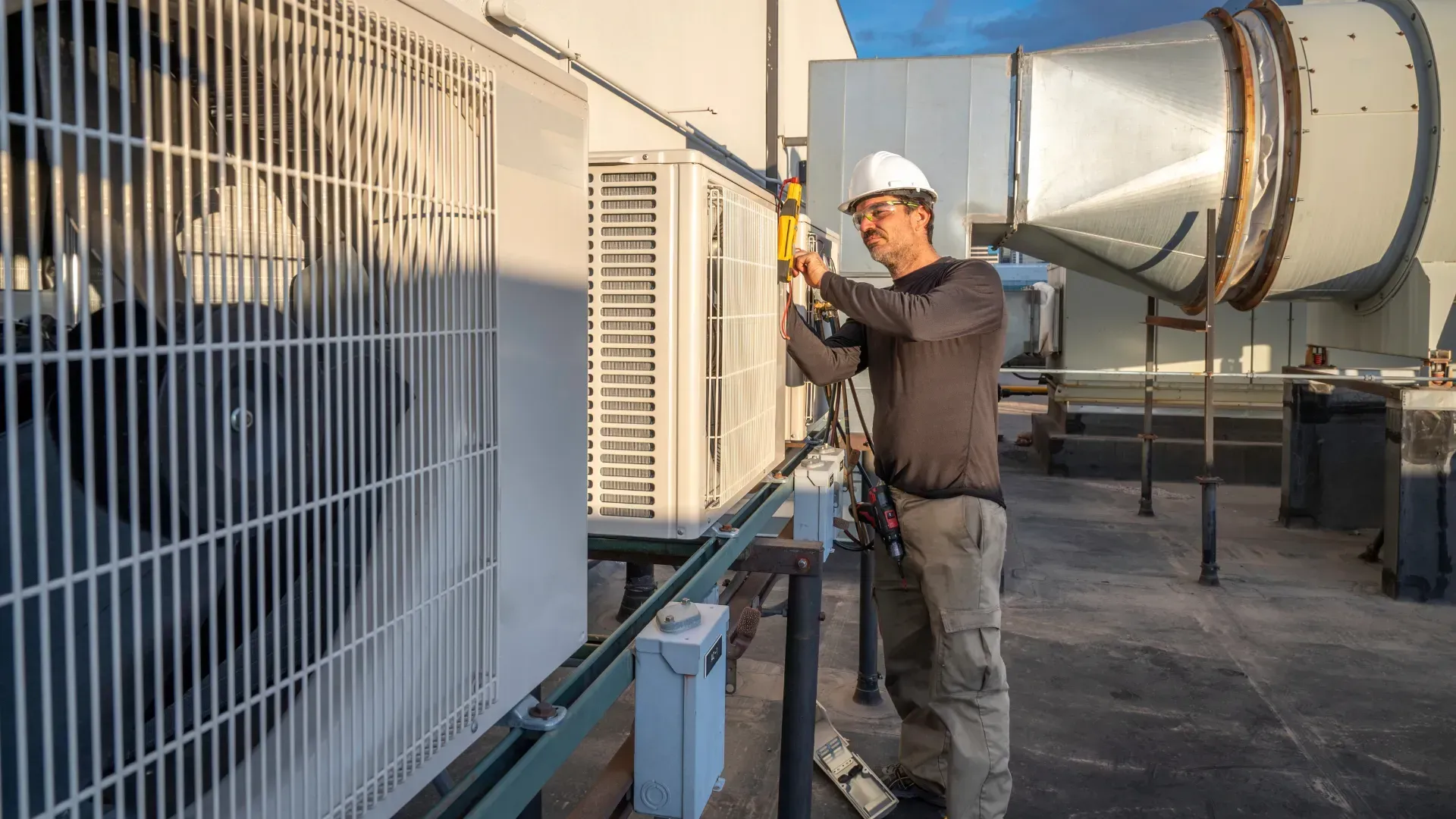 A man is working on an air conditioner on the roof of a building.