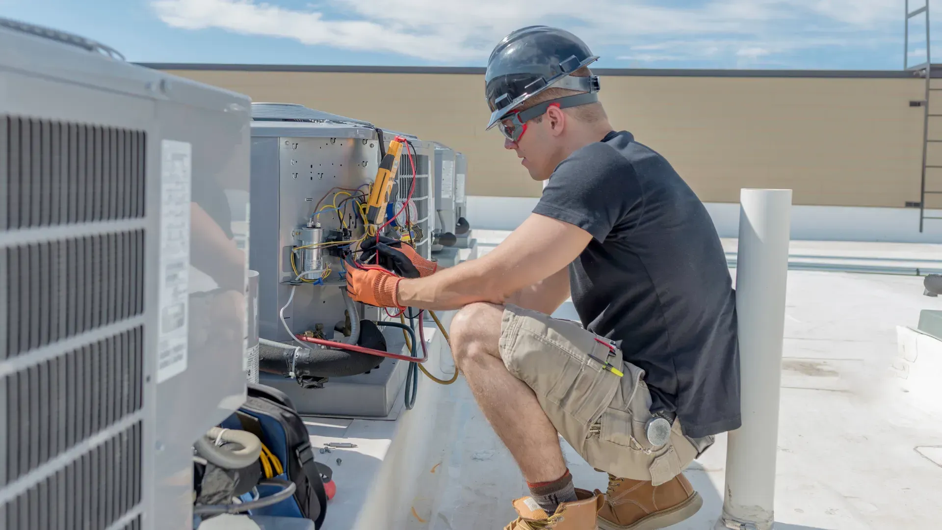 A man is working on an air conditioner on the roof of a building.