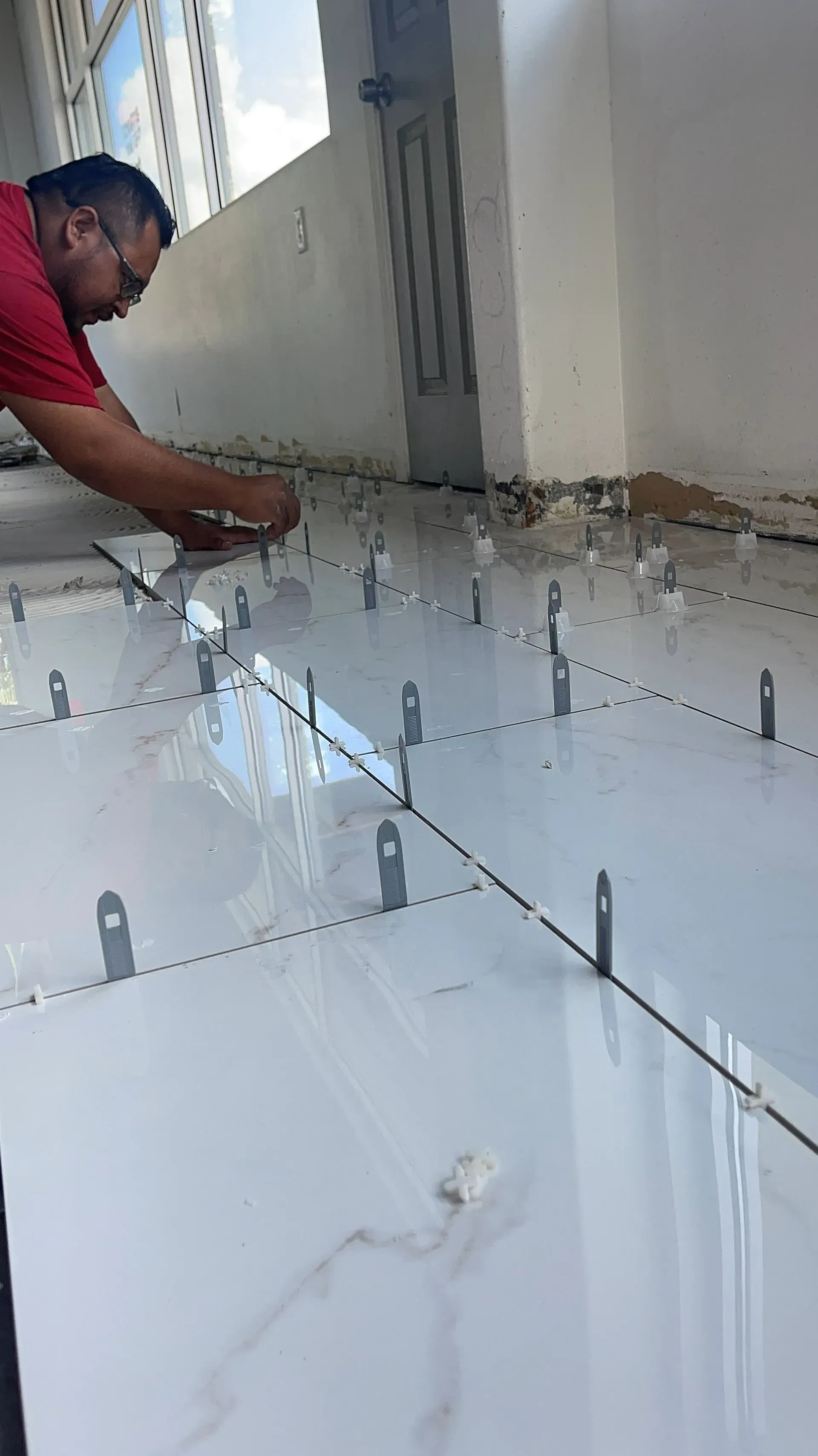 A man is laying tiles on the floor in a room.