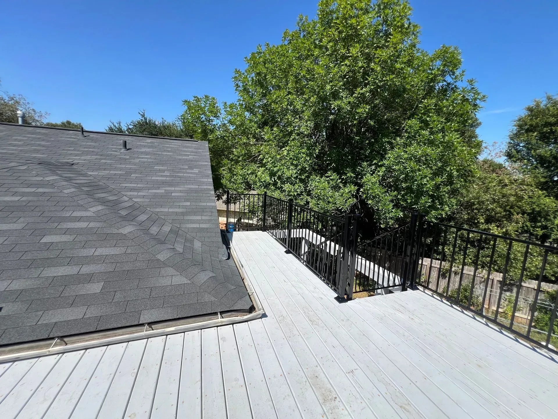 A white deck with a black roof and trees in the background.