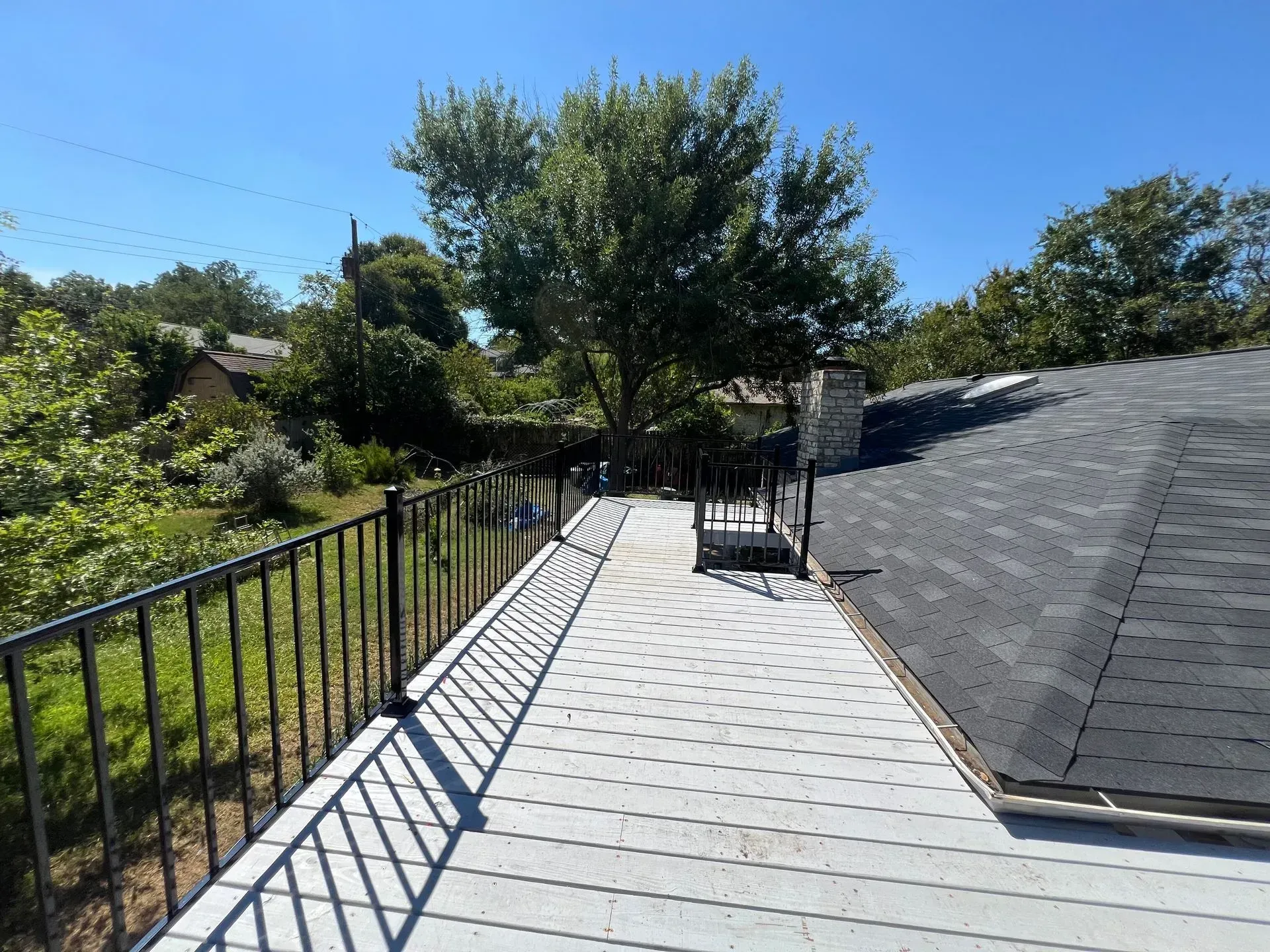 A rooftop deck with a metal railing and trees in the background.