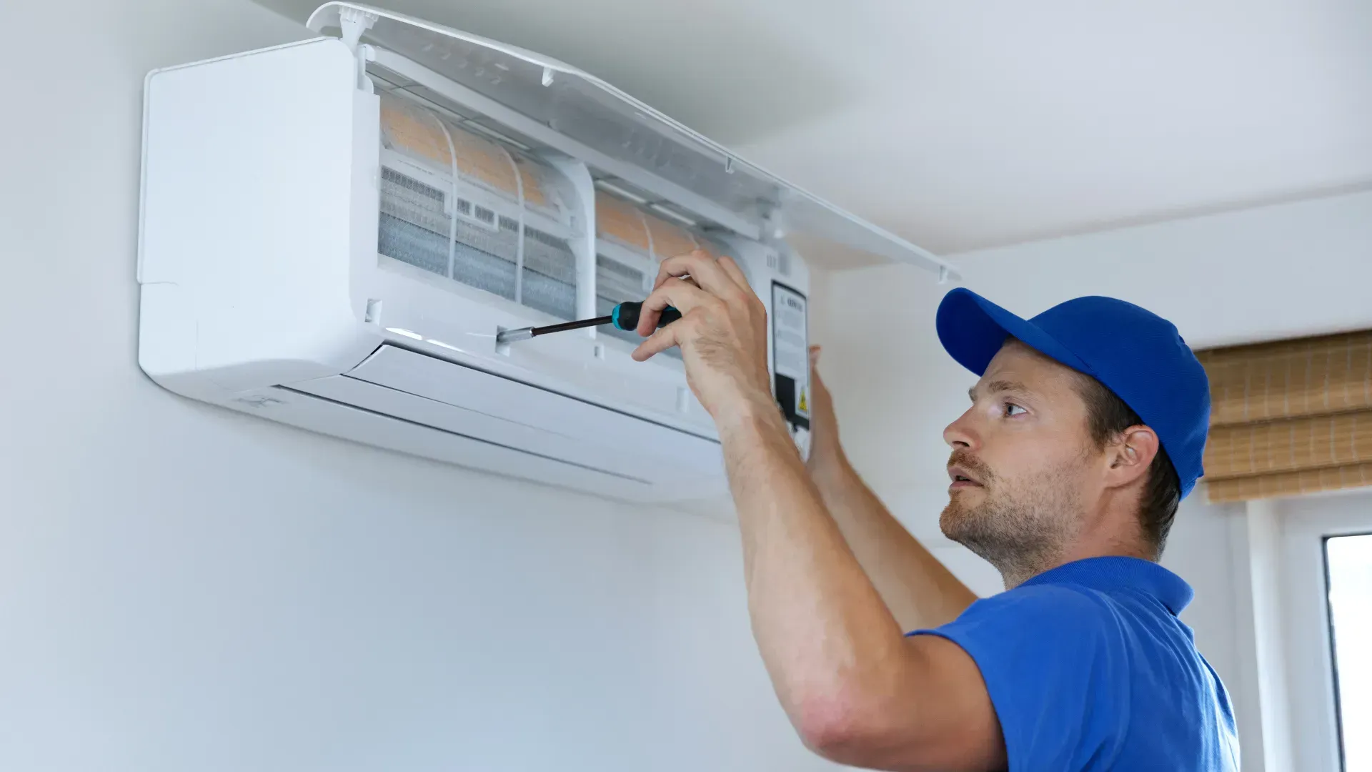 A man is fixing an air conditioner with a screwdriver.