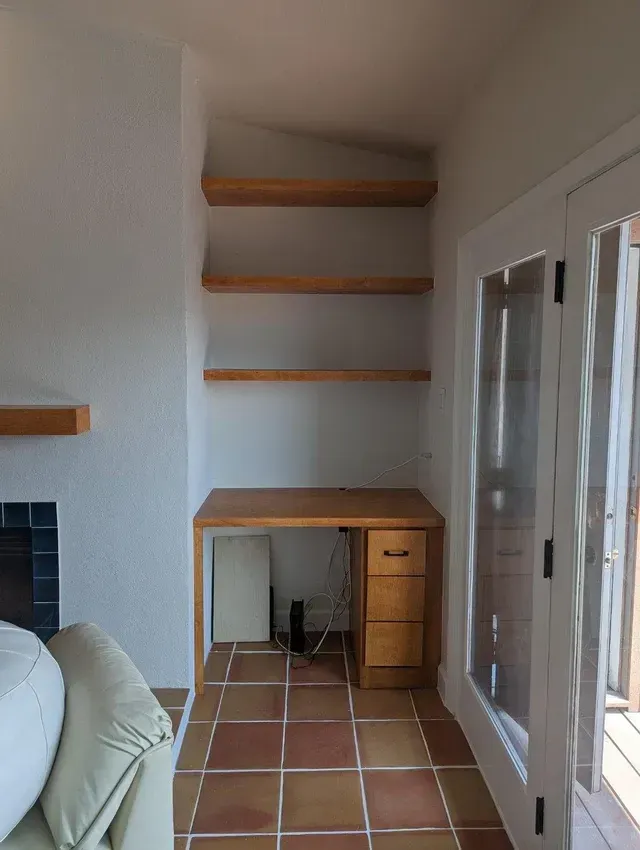 A living room with a desk and shelves and a fireplace