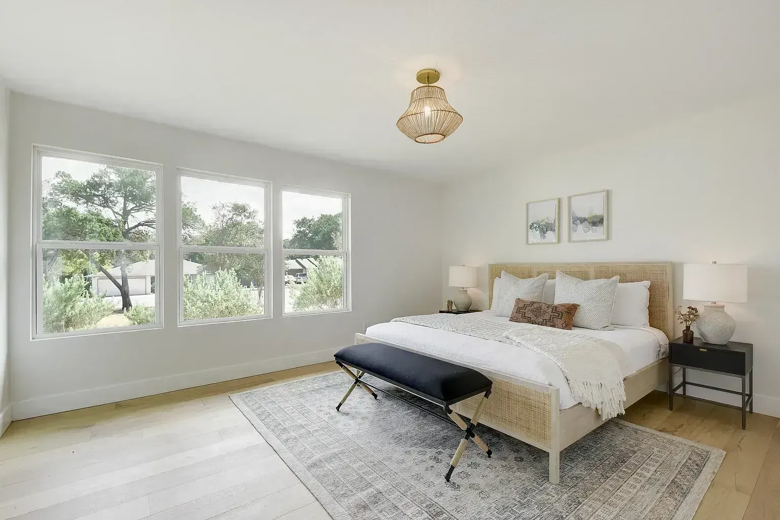 A bedroom with a large bed , a bench , lamps , and windows.