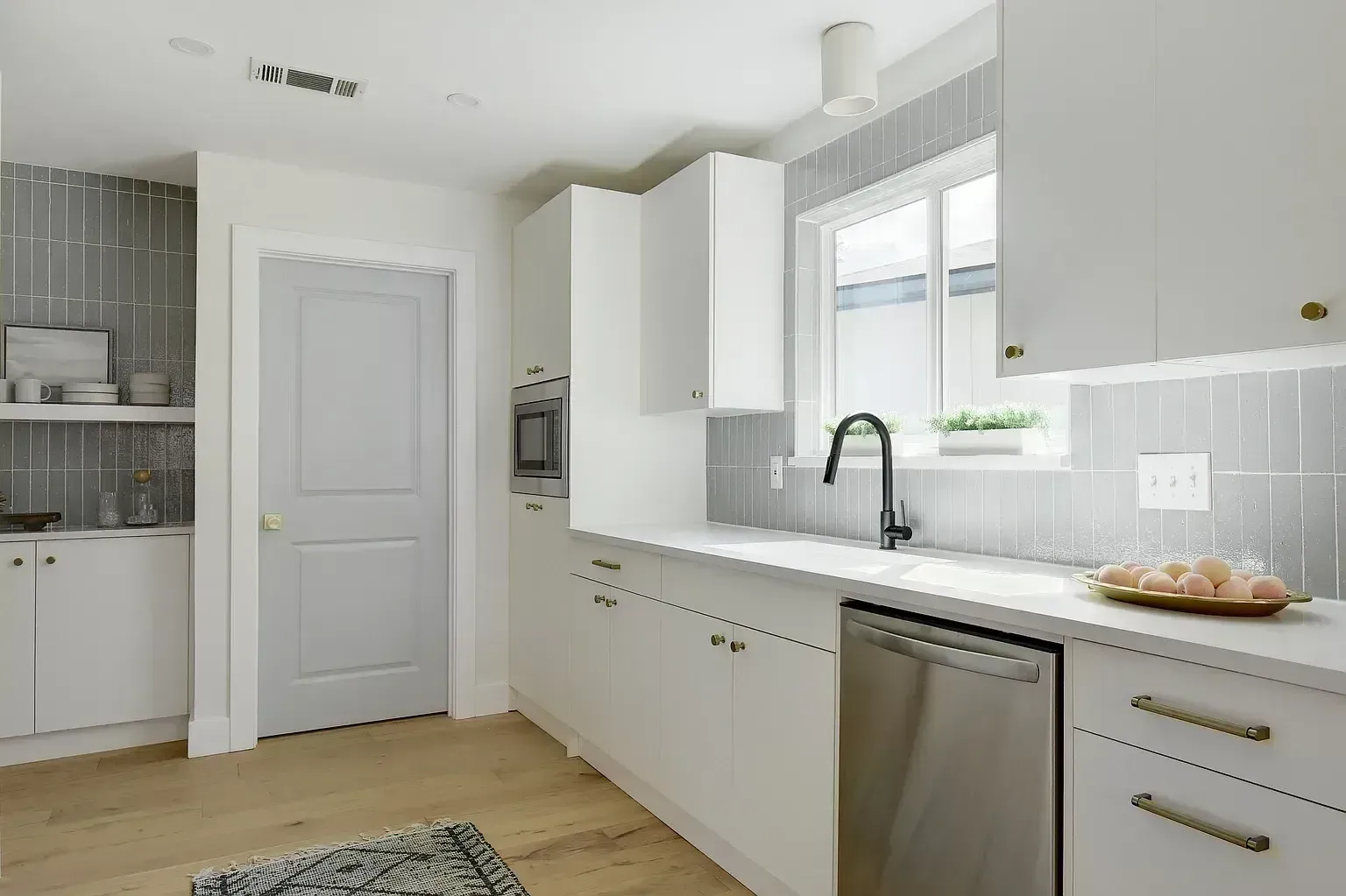 A kitchen with white cabinets , stainless steel appliances , a sink , and a window.