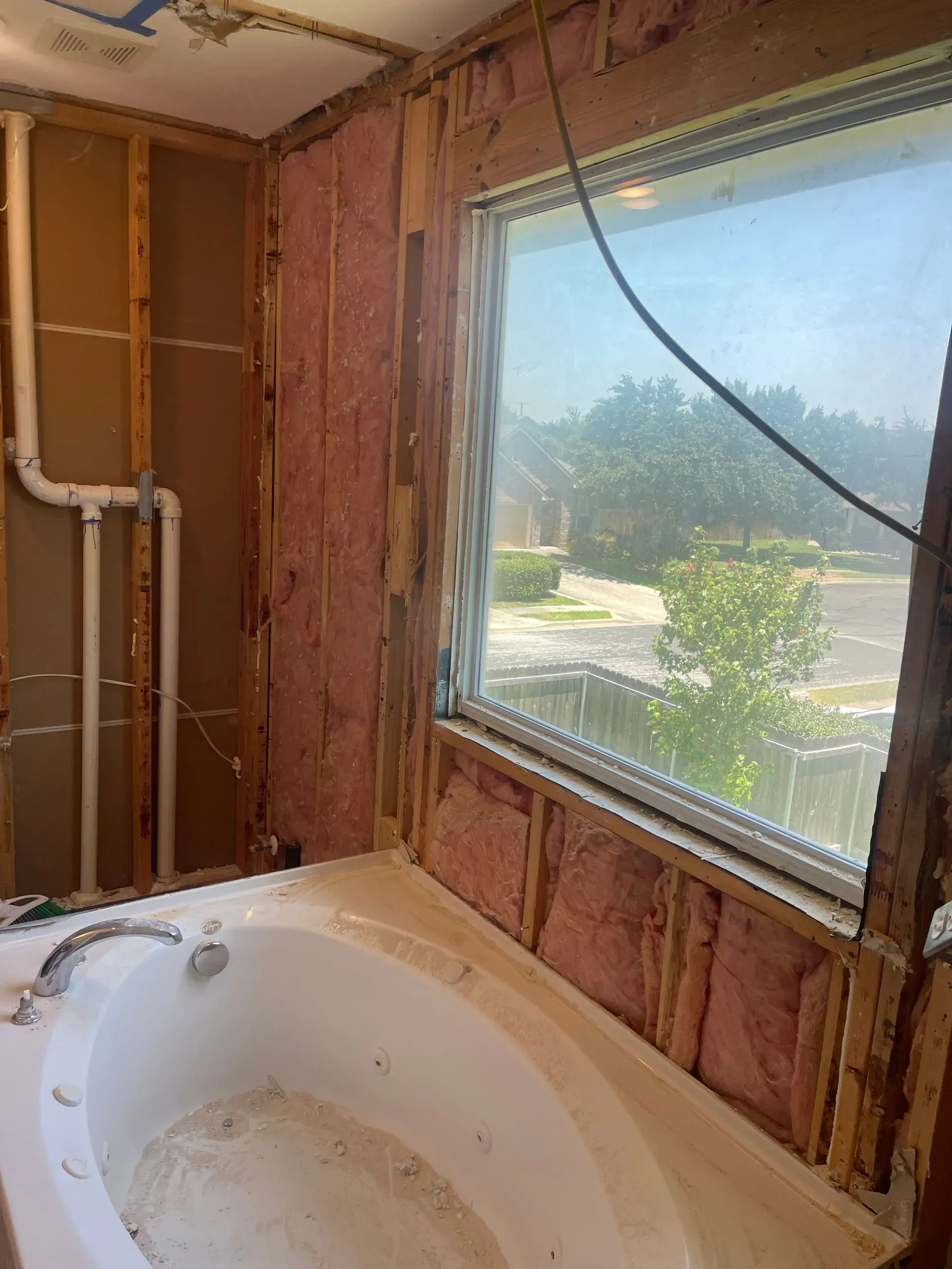 A bathtub in a bathroom under construction with a window.