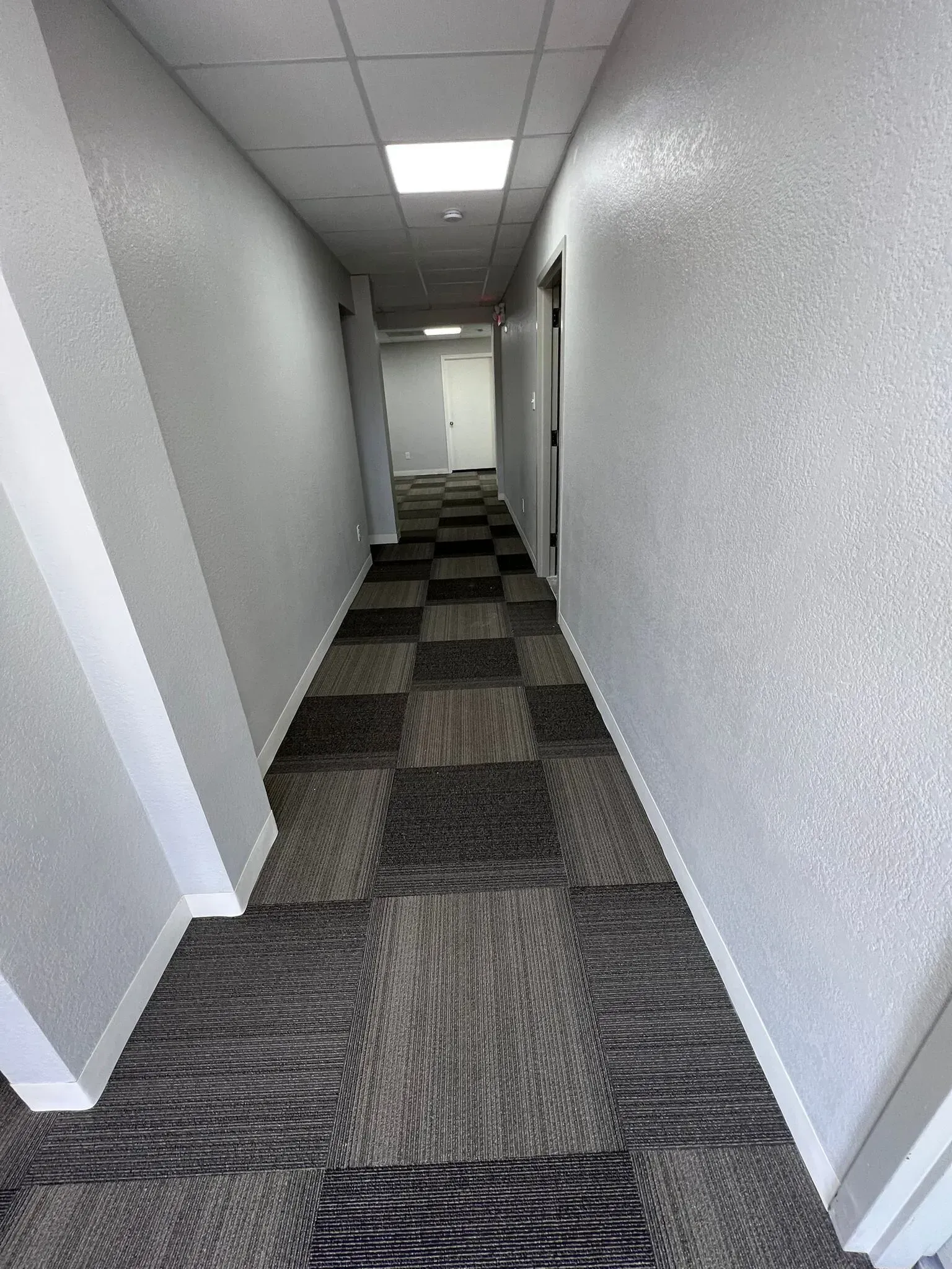 A long hallway with a checkered carpet and white walls.