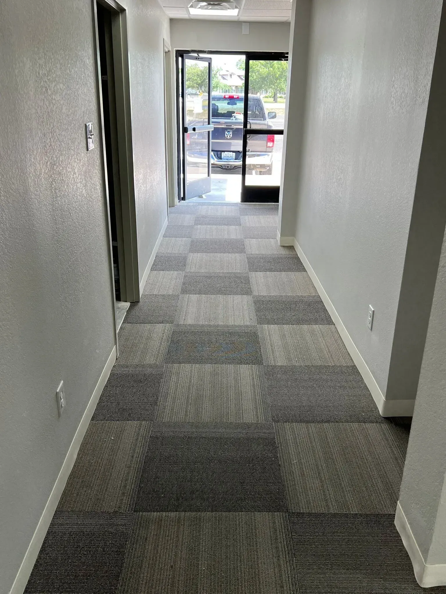 A long hallway with a checkered carpet and a car parked in the background.