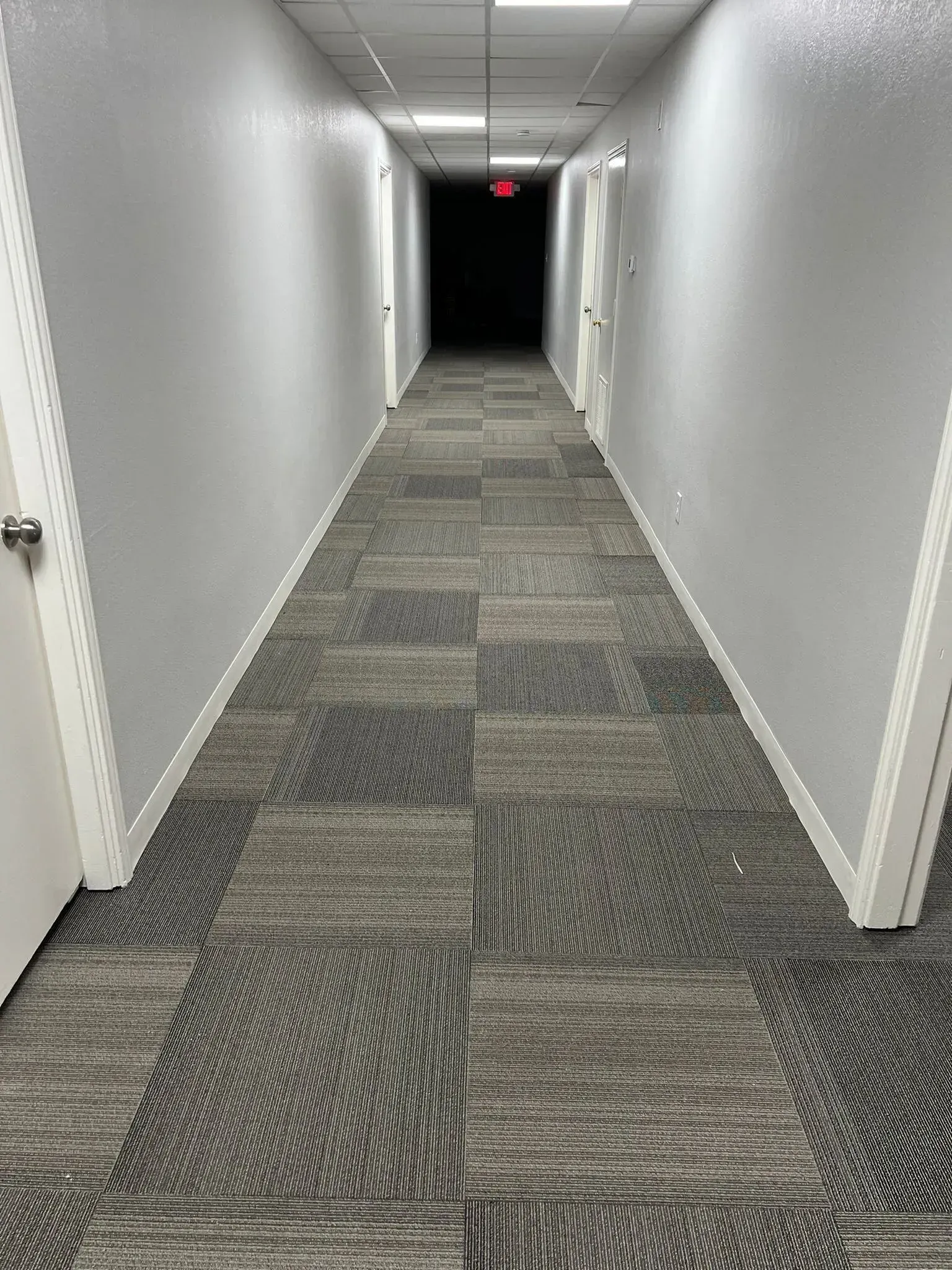 A long hallway with a carpeted floor and a red exit sign.