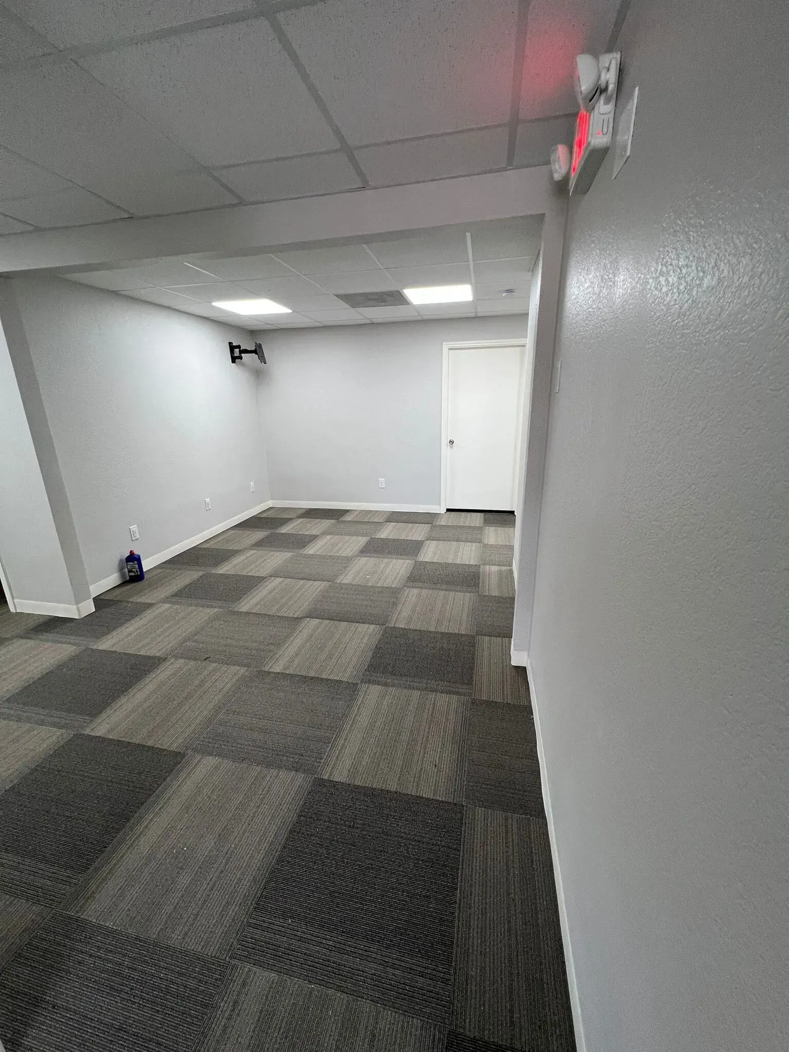 An empty room with a checkered carpet and a fire alarm on the wall.