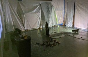 A room with a lot of trash on the floor and a white tarp on the wall.