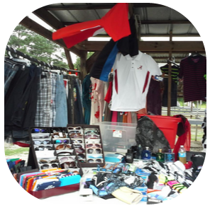 A flea market stall displaying hanging clothes, sunglasses, and assorted small items on a table under a covered structure.